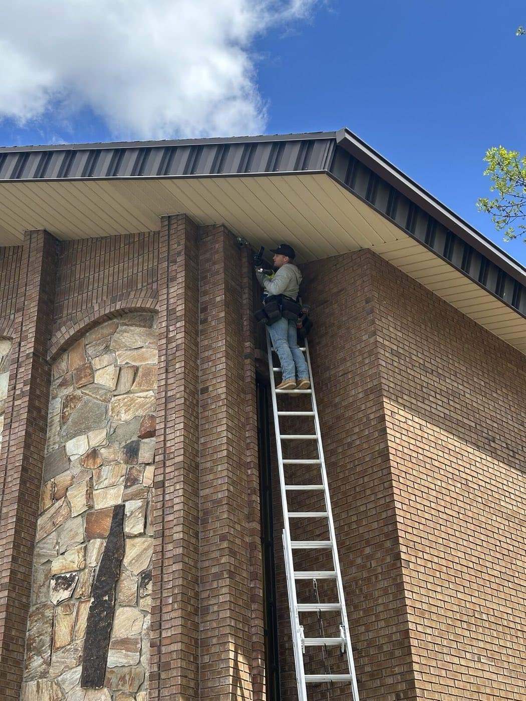 A technician on a ladder sealing an entry gap along a building's roofline