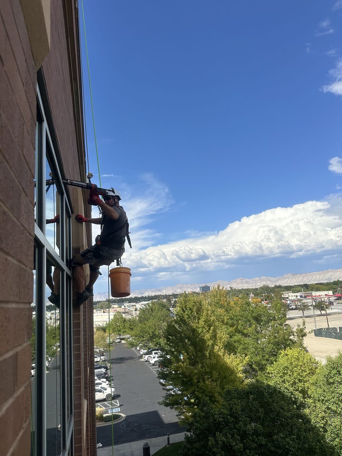 Colorado Wildlife Specialists technician rappelling a commercial building with a mountain ridge behind