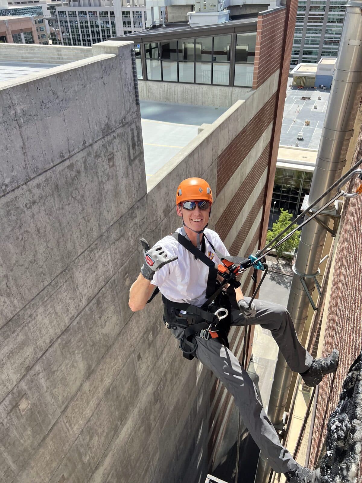 Two wildlife technicians in climbing harnesses giving a thumbs up after a rooftop exclusion job